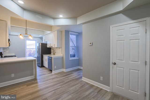 kitchen featuring pendant lighting, decorative backsplash, light wood-type flooring, white cabinetry, and stainless steel appliances