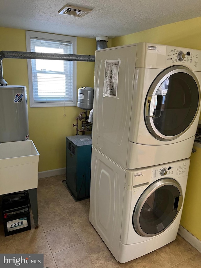 clothes washing area with stacked washer / drying machine, a textured ceiling, light tile patterned floors, and water heater