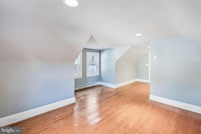 additional living space featuring vaulted ceiling, light wood-type flooring, and a baseboard radiator