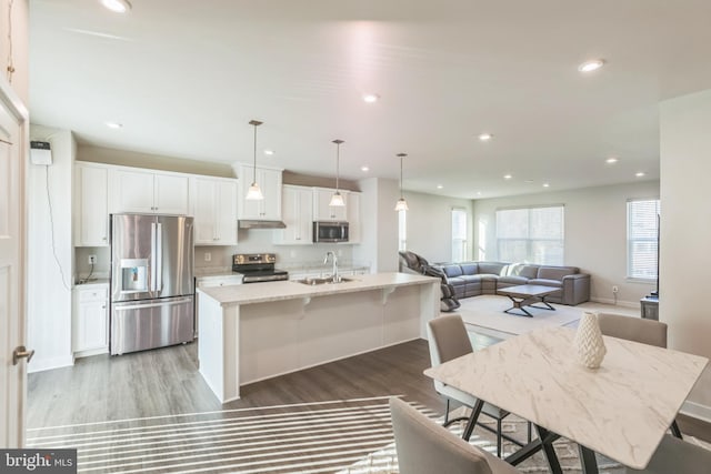 kitchen featuring a kitchen island with sink, hanging light fixtures, sink, appliances with stainless steel finishes, and white cabinetry