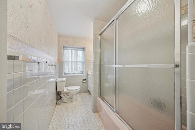 bathroom with combined bath / shower with glass door, toilet, and tile walls