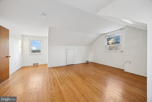 additional living space with cooling unit, light hardwood / wood-style floors, and lofted ceiling