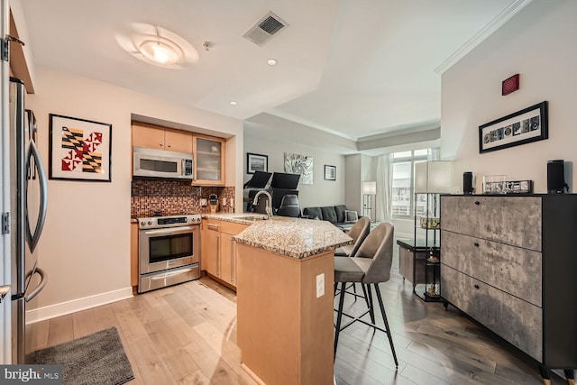 kitchen featuring stainless steel appliances, a breakfast bar, kitchen peninsula, light stone countertops, and light hardwood / wood-style flooring