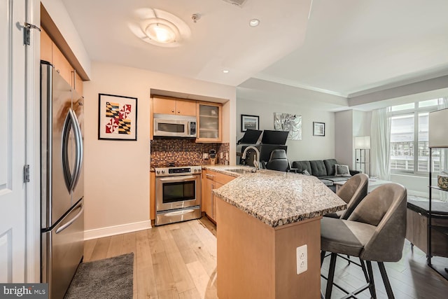 kitchen with light stone counters, stainless steel appliances, sink, kitchen peninsula, and light hardwood / wood-style flooring