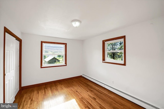 unfurnished bedroom with baseboard heating, light hardwood / wood-style floors, multiple windows, and a closet