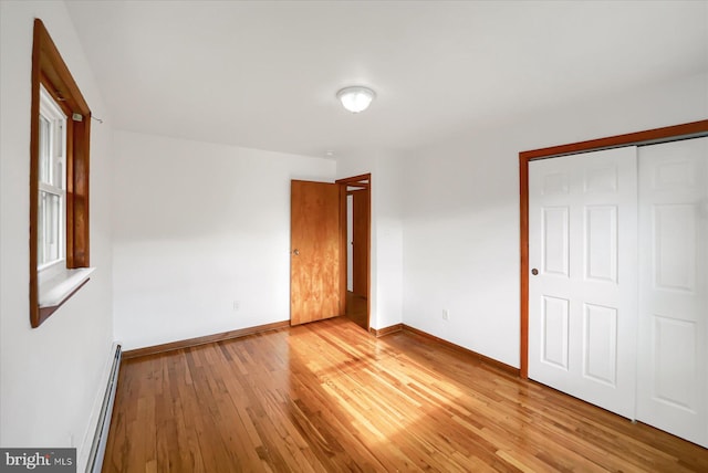 unfurnished bedroom with light hardwood / wood-style floors, baseboard heating, and a closet