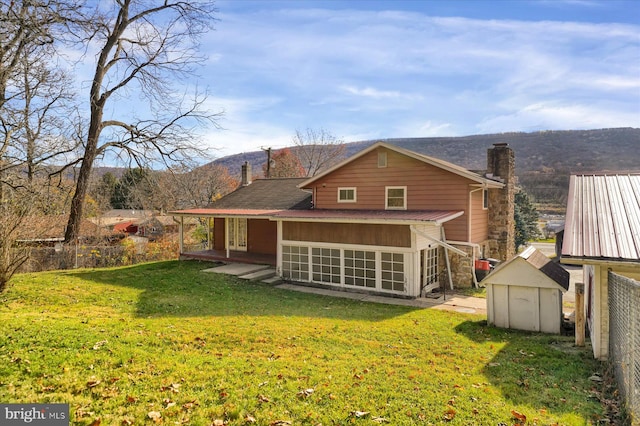 rear view of property with a shed, a mountain view, a sunroom, and a yard