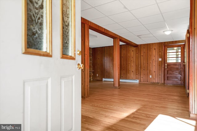 interior space with wood walls, a paneled ceiling, and light wood-type flooring