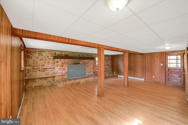 basement with baseboard heating, light wood-type flooring, a paneled ceiling, and wood walls