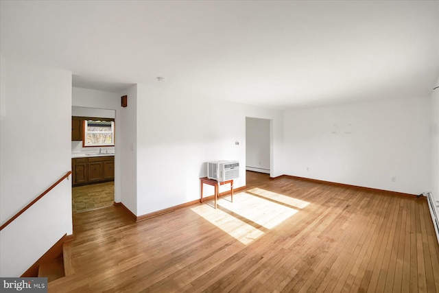 empty room with a baseboard heating unit, sink, light hardwood / wood-style flooring, and an AC wall unit