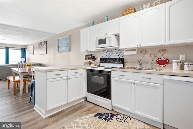 kitchen with white cabinets, white appliances, sink, and light hardwood / wood-style floors