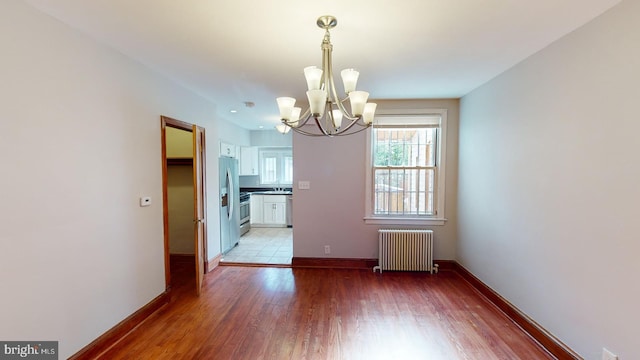 unfurnished dining area with wood-type flooring, sink, a chandelier, and radiator