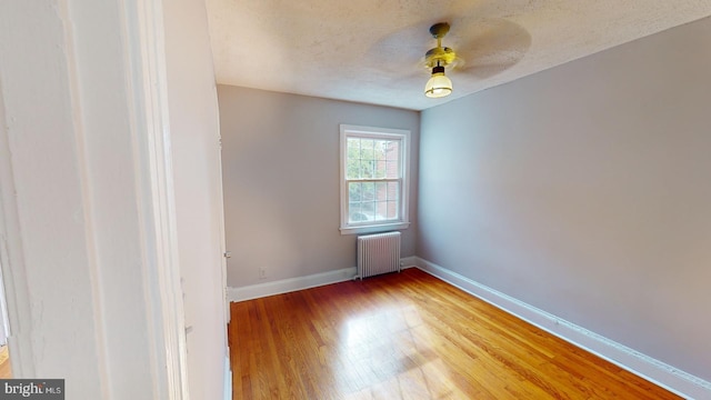 spare room featuring a textured ceiling, hardwood / wood-style flooring, ceiling fan, and radiator