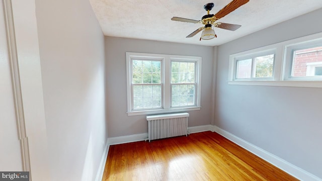 spare room with radiator heating unit, hardwood / wood-style floors, ceiling fan, and a textured ceiling