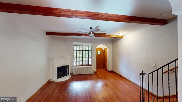 unfurnished living room with radiator, light hardwood / wood-style flooring, ceiling fan, beam ceiling, and a large fireplace