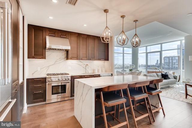 kitchen with a kitchen bar, sink, stainless steel stove, light wood-type flooring, and decorative light fixtures