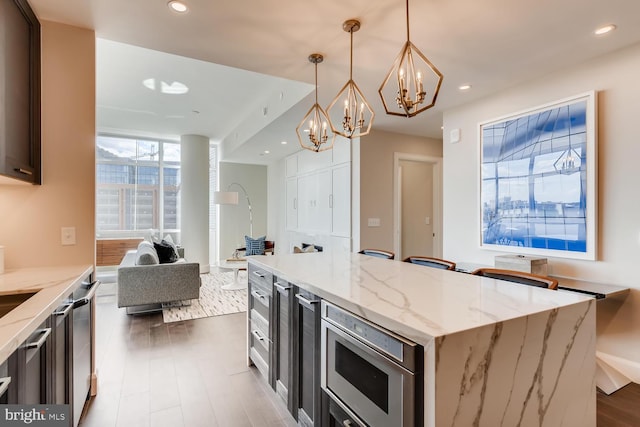 kitchen with appliances with stainless steel finishes, light stone counters, hardwood / wood-style floors, a center island, and pendant lighting