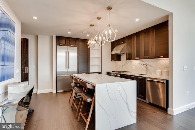 kitchen featuring stainless steel appliances, a kitchen island, backsplash, decorative light fixtures, and dark hardwood / wood-style floors