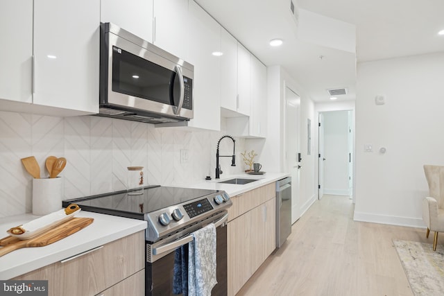 kitchen featuring sink, tasteful backsplash, light hardwood / wood-style floors, white cabinets, and appliances with stainless steel finishes