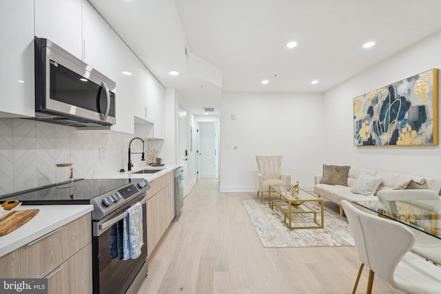 kitchen featuring appliances with stainless steel finishes, backsplash, sink, white cabinets, and light hardwood / wood-style floors