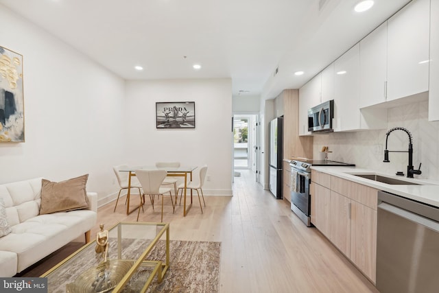 kitchen featuring decorative backsplash, stainless steel appliances, sink, light hardwood / wood-style floors, and white cabinetry