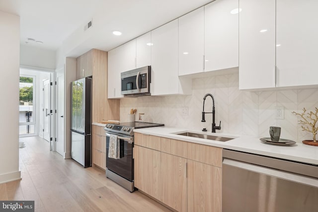 kitchen with appliances with stainless steel finishes, light brown cabinetry, sink, light hardwood / wood-style flooring, and white cabinets