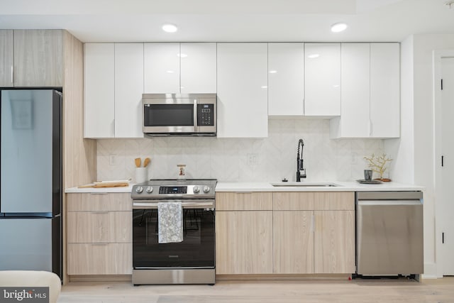 kitchen with light brown cabinetry, light wood-type flooring, stainless steel appliances, sink, and white cabinets