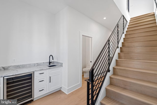 bar featuring light stone counters, beverage cooler, white cabinets, sink, and light wood-type flooring