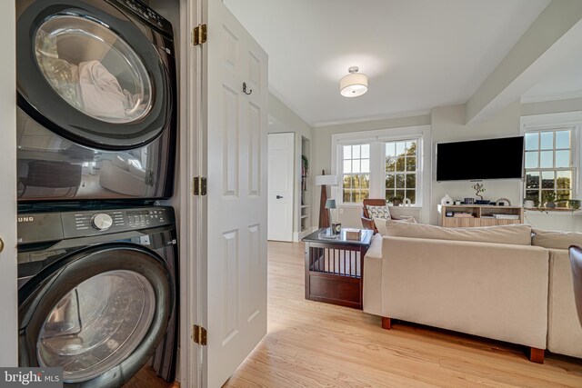 laundry room with ornamental molding, stacked washer and dryer, and light wood-type flooring