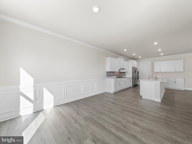 kitchen with wood-type flooring, white cabinets, a kitchen island with sink, and stainless steel fridge