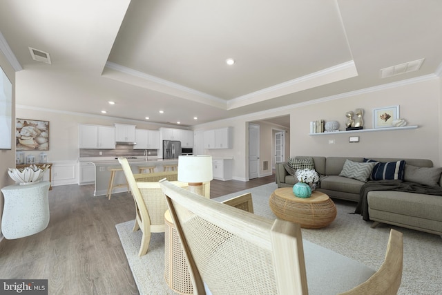 living room featuring a raised ceiling, crown molding, and light wood-type flooring