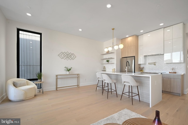 kitchen with stainless steel refrigerator, a center island with sink, white cabinetry, a kitchen breakfast bar, and hanging light fixtures