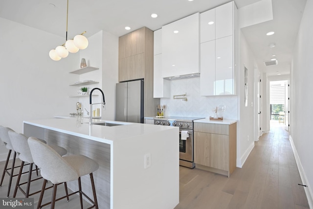 kitchen with light wood-type flooring, appliances with stainless steel finishes, pendant lighting, sink, and white cabinets