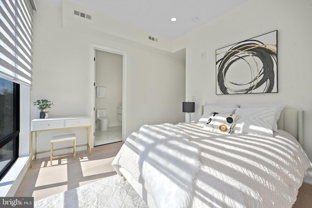 bedroom with light wood-type flooring, multiple windows, and ensuite bath