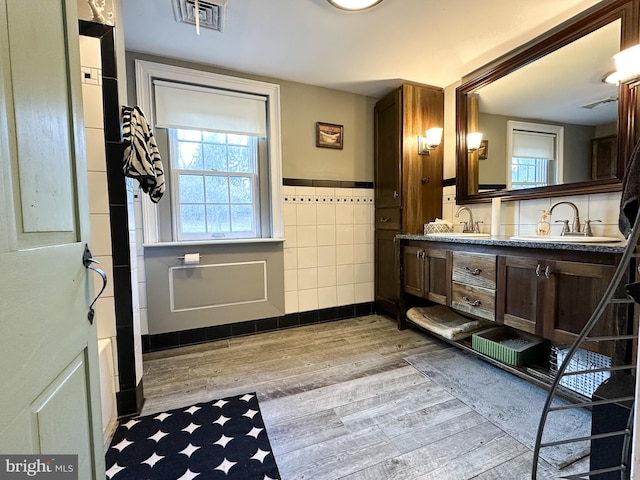 bathroom with a bath, vanity, hardwood / wood-style flooring, and tile walls