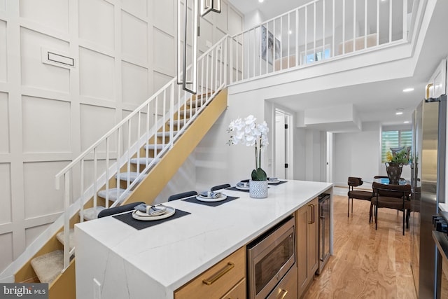 kitchen with light stone counters, beverage cooler, stainless steel microwave, a center island, and light wood-type flooring