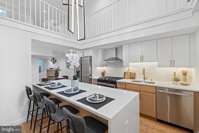 kitchen with white cabinetry, wall chimney range hood, appliances with stainless steel finishes, sink, and light hardwood / wood-style floors