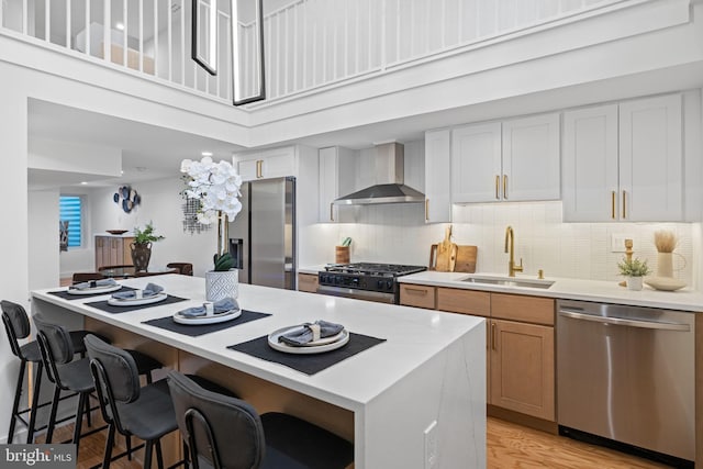 kitchen featuring sink, appliances with stainless steel finishes, white cabinets, wall chimney range hood, and light wood-type flooring