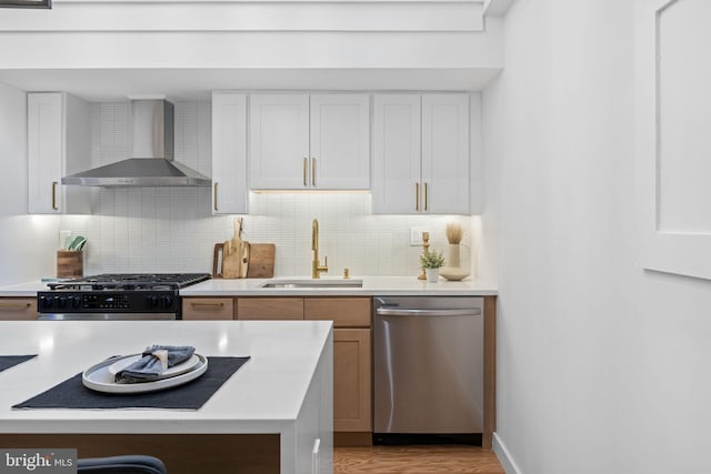 kitchen featuring stainless steel appliances, backsplash, white cabinetry, sink, and wall chimney exhaust hood