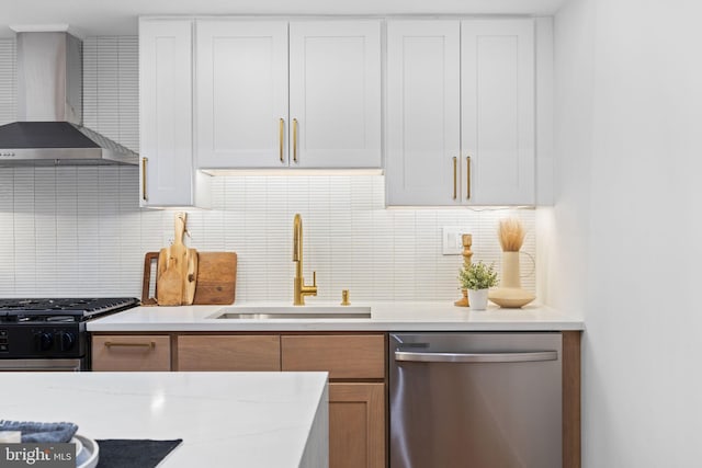 kitchen featuring stainless steel appliances, white cabinetry, sink, light stone countertops, and wall chimney range hood