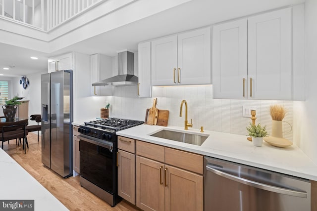 kitchen with light hardwood / wood-style floors, sink, appliances with stainless steel finishes, wall chimney exhaust hood, and white cabinets