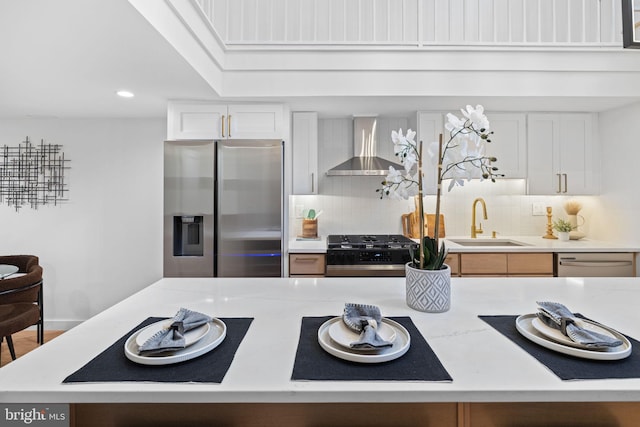 kitchen featuring white cabinetry, sink, appliances with stainless steel finishes, wall chimney range hood, and decorative backsplash