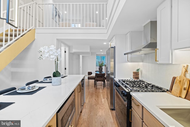 kitchen featuring stainless steel appliances, light hardwood / wood-style floors, wall chimney range hood, backsplash, and white cabinetry