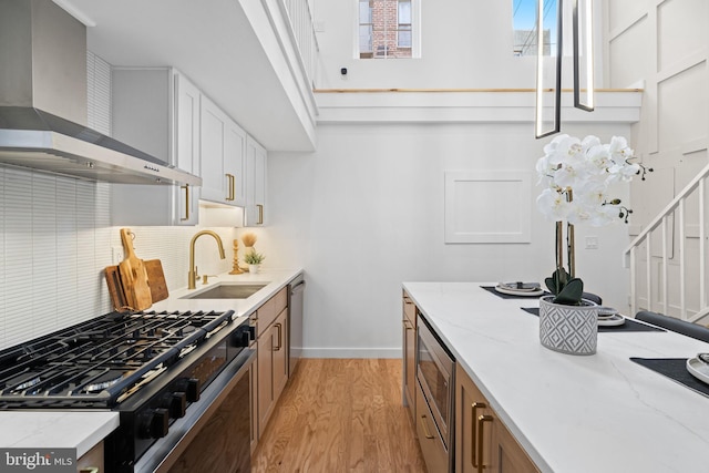 kitchen featuring white cabinetry, wall chimney range hood, appliances with stainless steel finishes, sink, and light hardwood / wood-style flooring