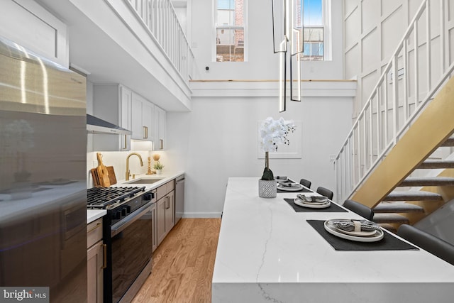 kitchen with white cabinets, light hardwood / wood-style flooring, sink, extractor fan, and appliances with stainless steel finishes