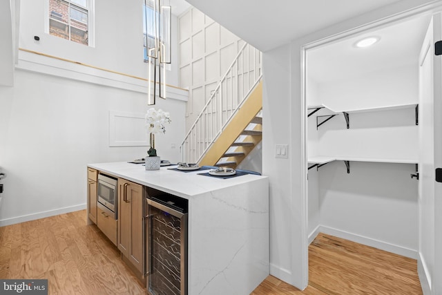 bar with light wood-type flooring, stainless steel microwave, and wine cooler