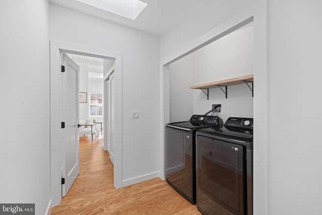 washroom featuring washer and clothes dryer, a skylight, and light hardwood / wood-style floors