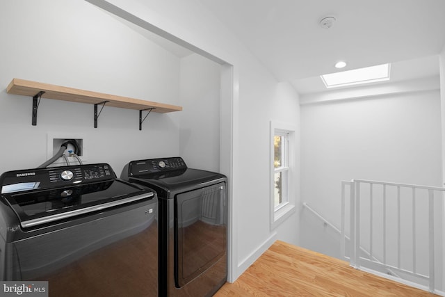 laundry room with wood-type flooring, a skylight, and washing machine and clothes dryer