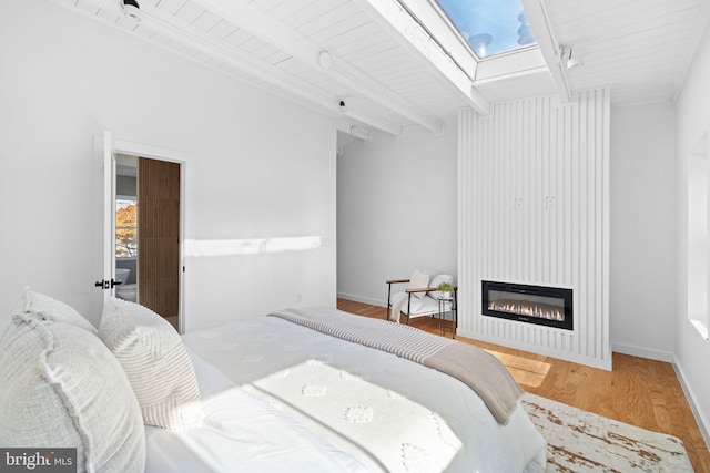 bedroom featuring wooden ceiling, beamed ceiling, a skylight, hardwood / wood-style floors, and a fireplace