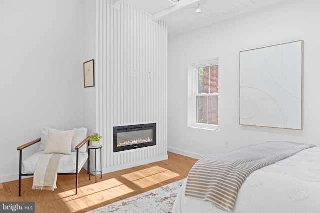 bedroom with hardwood / wood-style floors, a fireplace, beam ceiling, and wooden ceiling